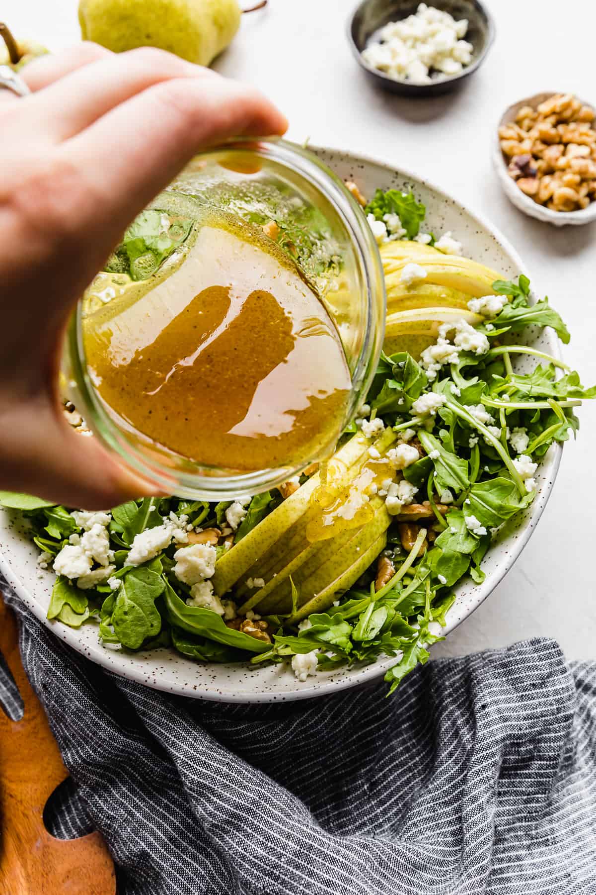 Salad dressing being poured over a Rocket and Pear Salad in a large bowl.