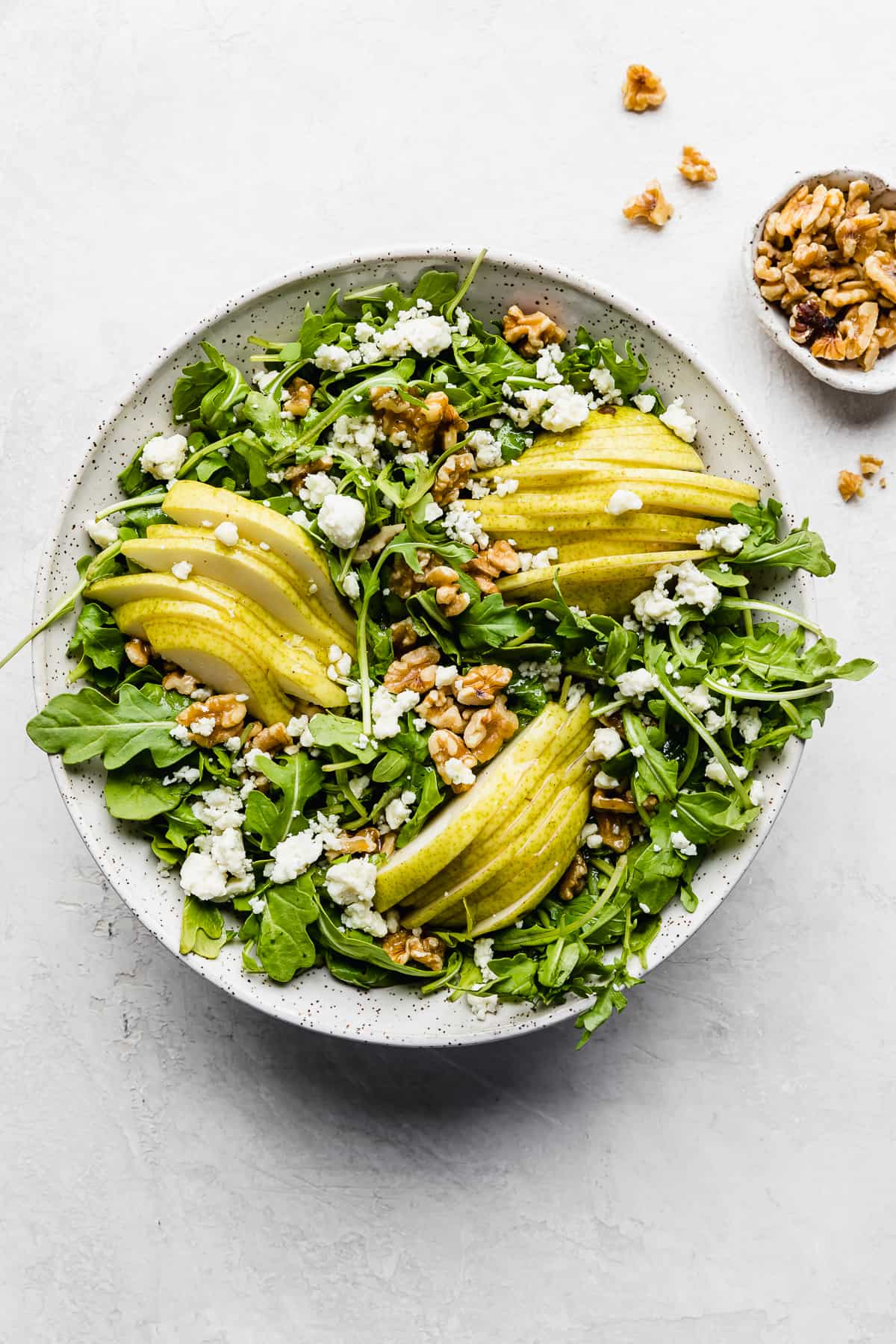 Rocket and Pear Salad on a white background with walnuts scattered around the bowl.
