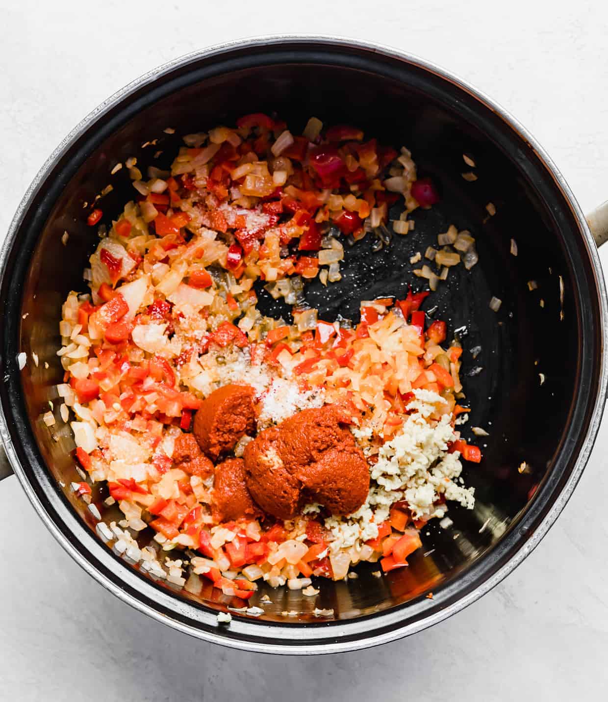 A black pot with cooked diced onion, red pepper, and red curry past in it.