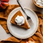 Overhead photo of a slice of whipped cream topped Crustless Pumpkin Pie on a plate with a fork to the side.