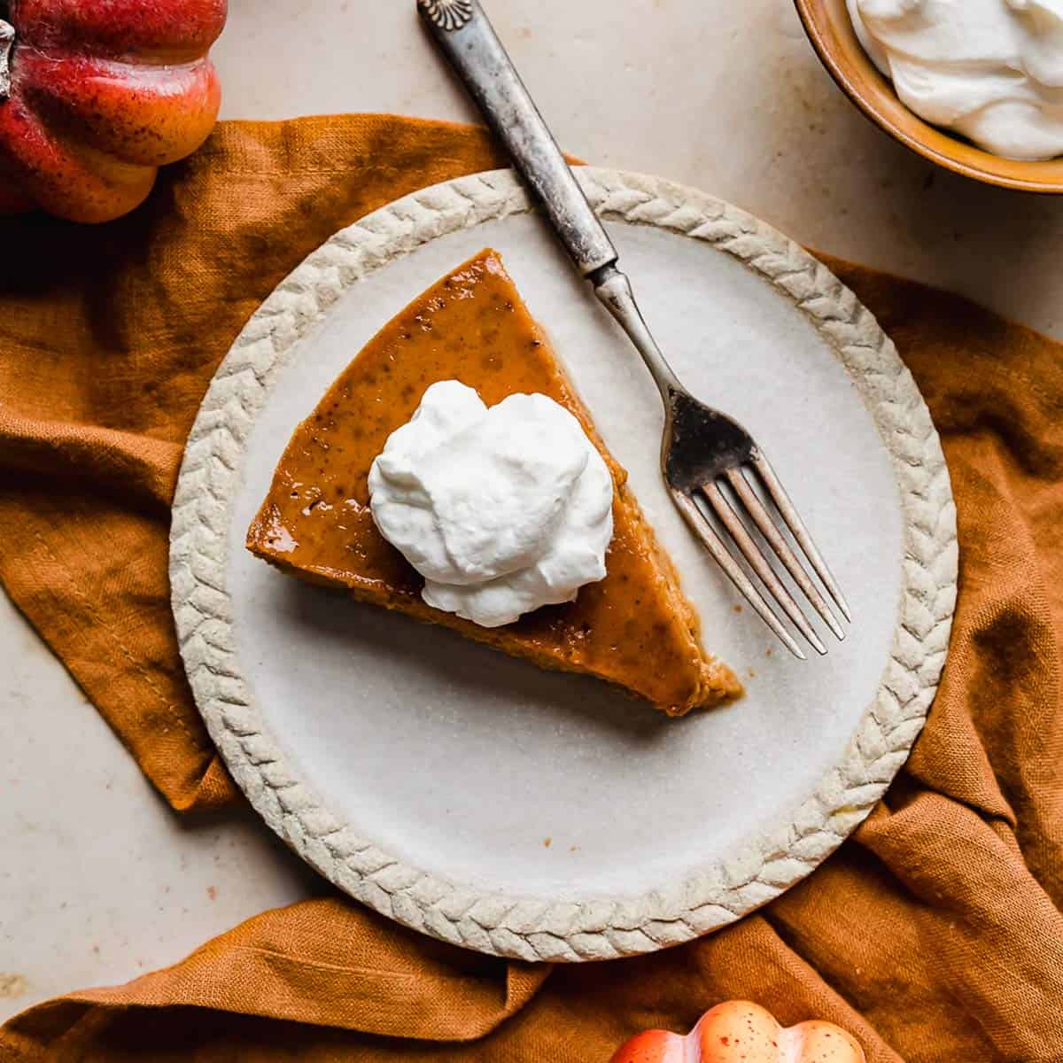 Overhead photo of a slice of whipped cream topped Crustless Pumpkin Pie on a plate with a fork to the side.