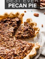 A slice of pecan pie in a pie plate with pecans around the pie.