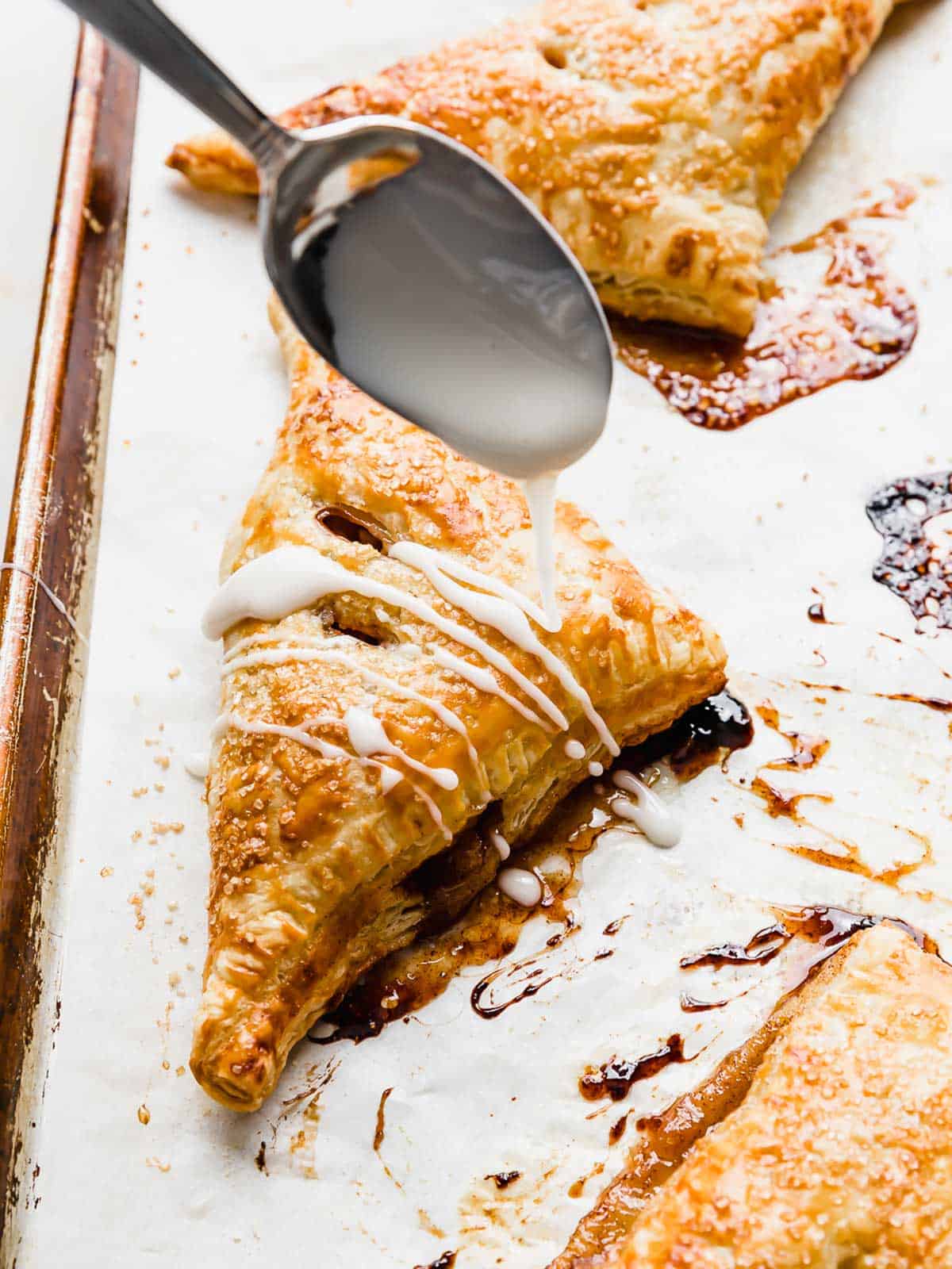 A spoon drizzling glaze overtop a Puff Pastry Apple Turnover.