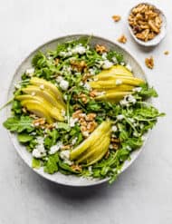 Rocket and Pear Salad in a large bowl with a small bowl of walnuts on the side.