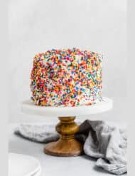 A sprinkle covered Smash Cake Recipe on a white marbled cake stand.