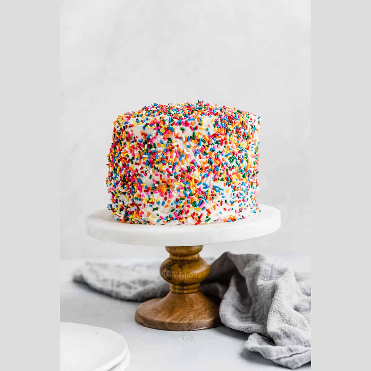 A sprinkle covered Smash Cake Recipe on a white marbled cake stand.