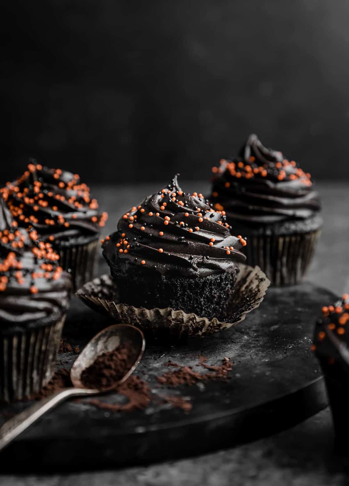 Black Velvet Cupcakes topped with orange sprinkles on a black plate against a black background.