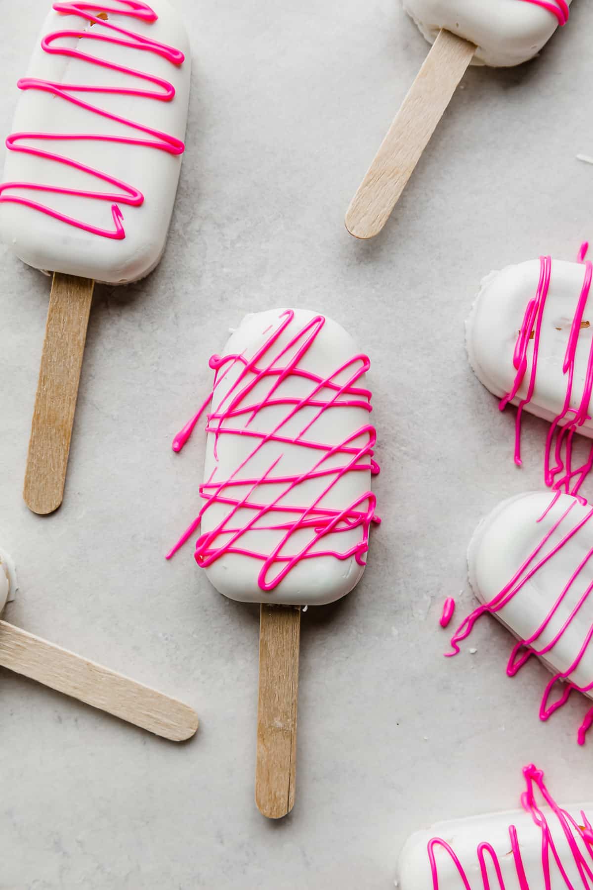 White chocolate covered Cakesicles drizzled with hot pink chocolate, on a white background. 