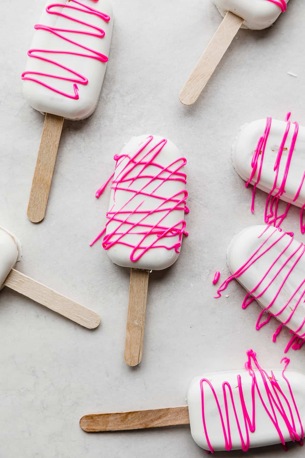 White chocolate Cakesicles drizzled with hot pink chocolate, on a white background.