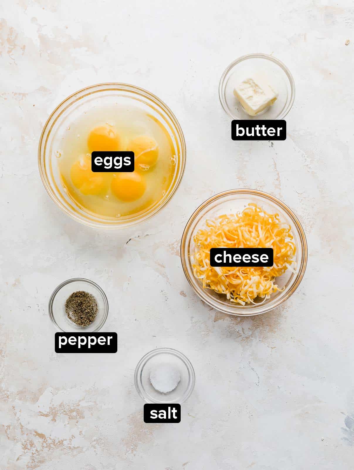 Ingredients used to make Cheesy Scrambled Eggs on a textured white background.