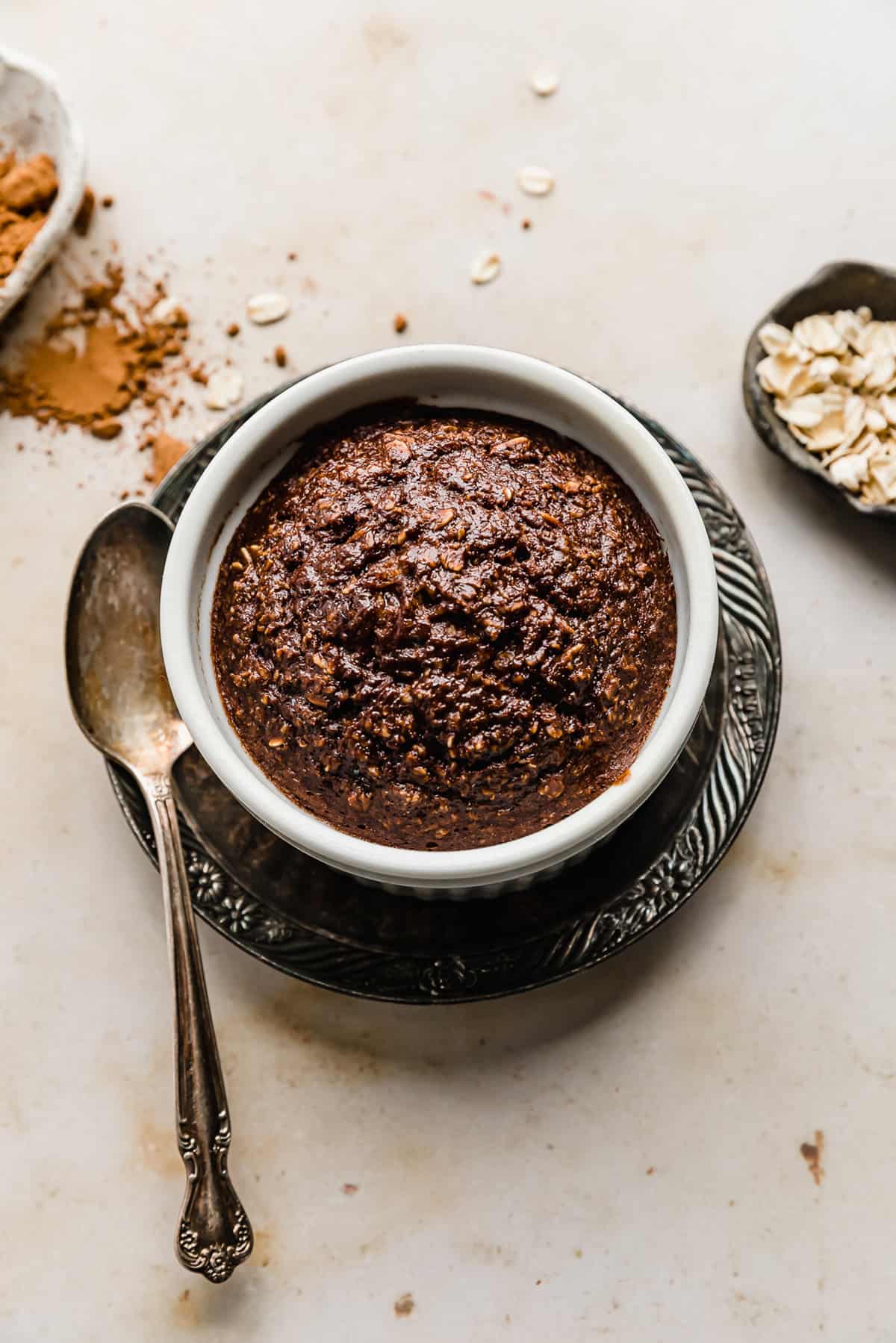 Chocolate Baked Oats in a white ramekin on a brown plate.