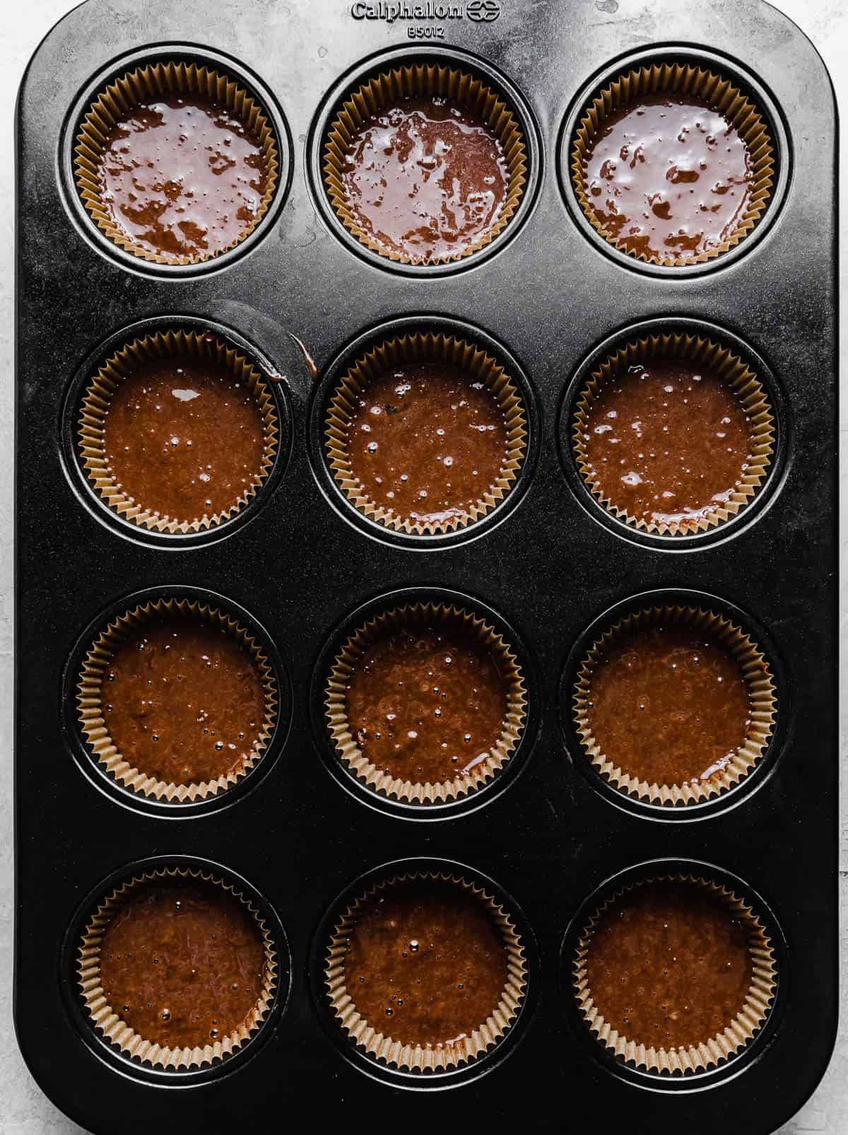 A twelve cupcake pan with tan cupcake liners filled with chocolate batter.