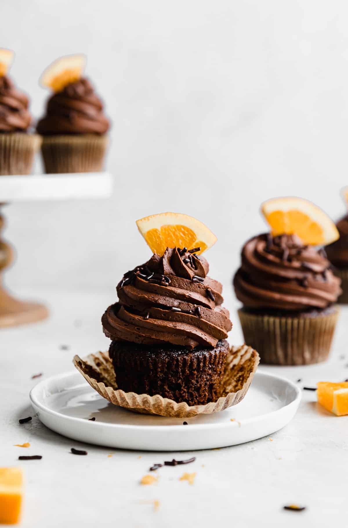 Chocolate frosting topped Chocolate Orange Cupcakes with a fresh orange slice stuck into the frosting, on a white background.