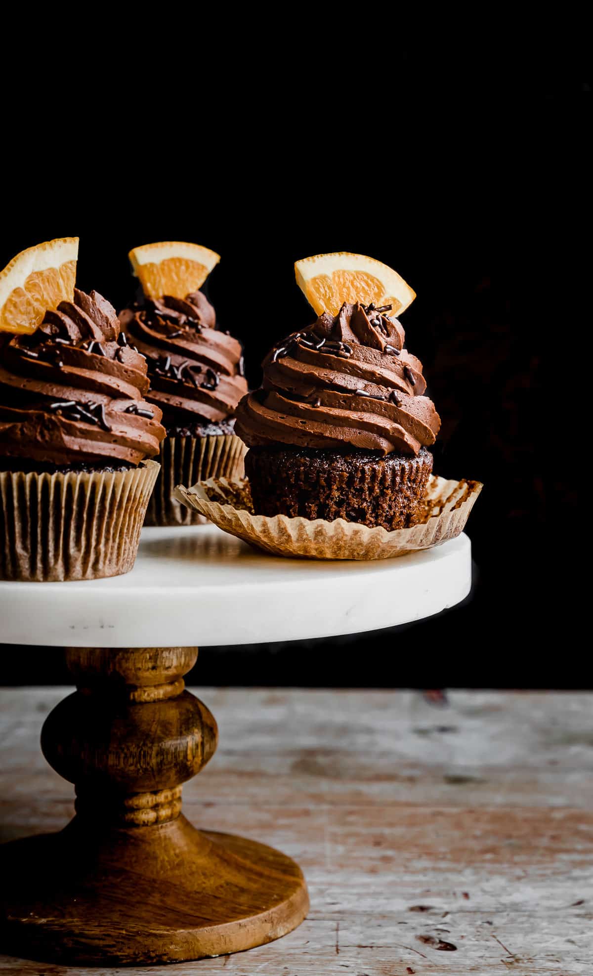 Chocolate Orange Cupcakes on a white marble topped cake stand against a black background.