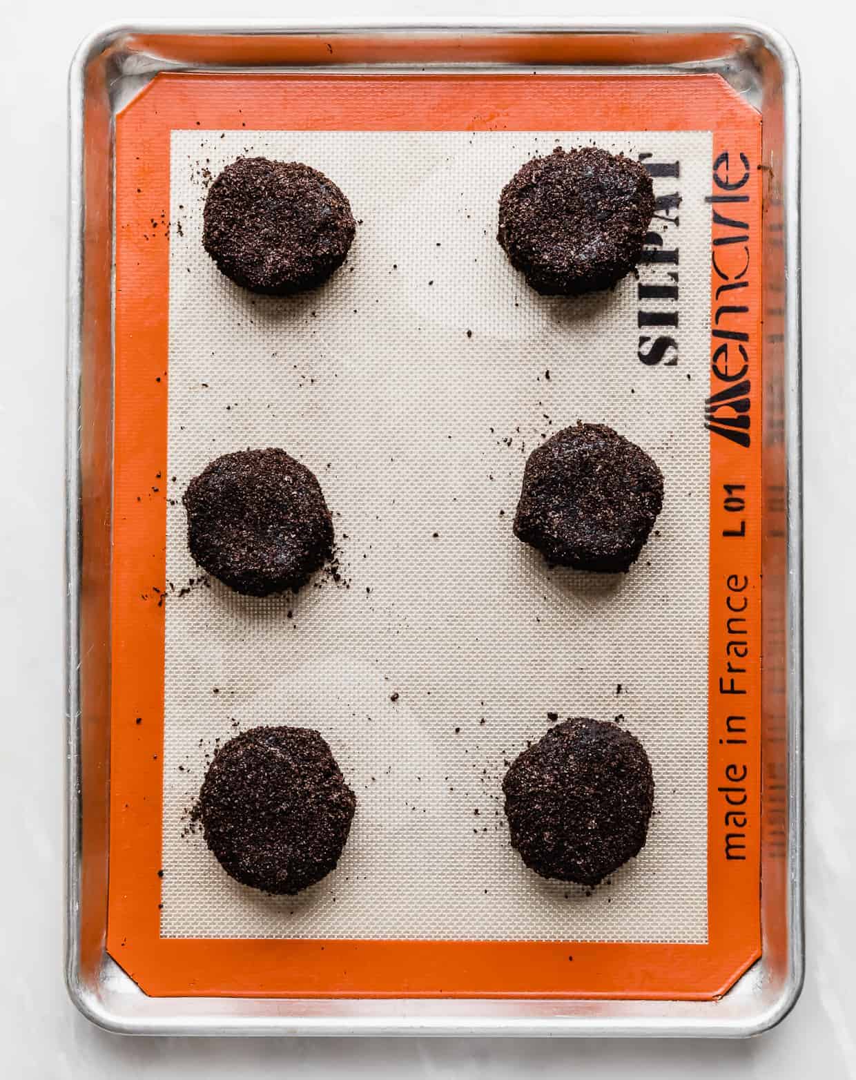 Six Crumbl Chocolate Oreo Cookie dough balls on a baking sheet.