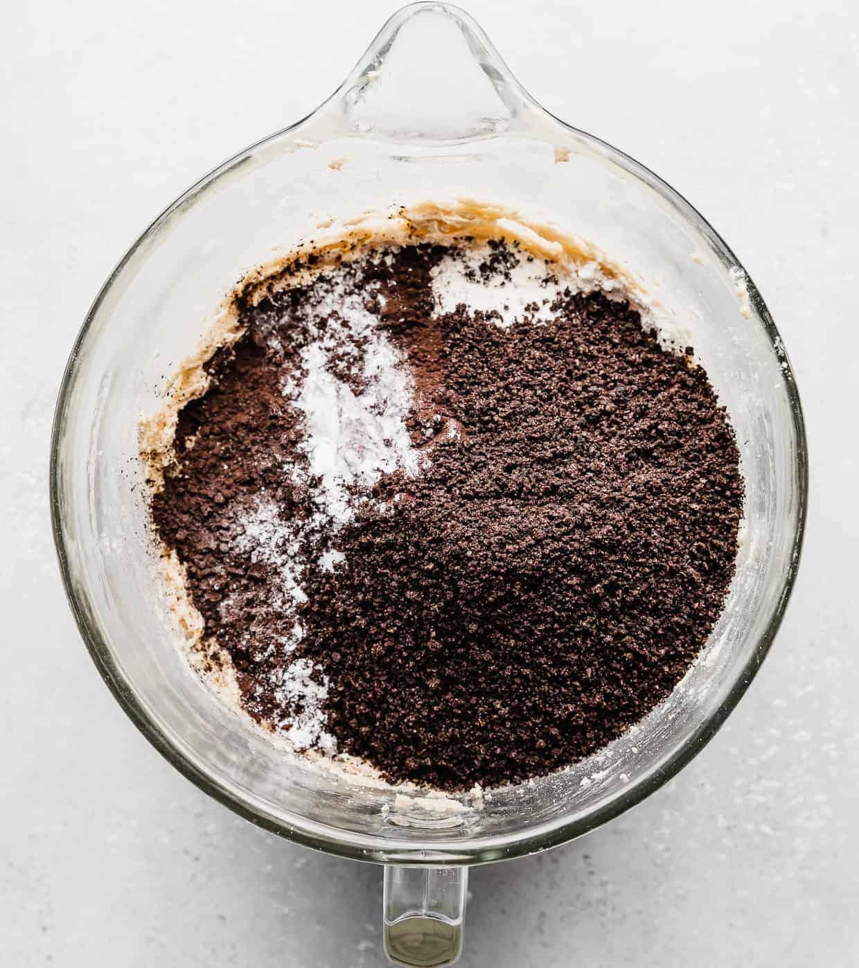A mixing bowl with crushed Oreos, black cocoa powder, and flour overtop creamed butter.