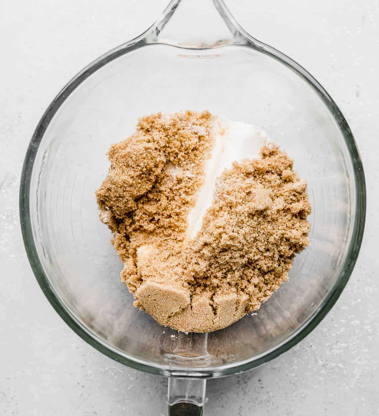 A glass mixing bowl with brown sugar, sugar, and butter in it.