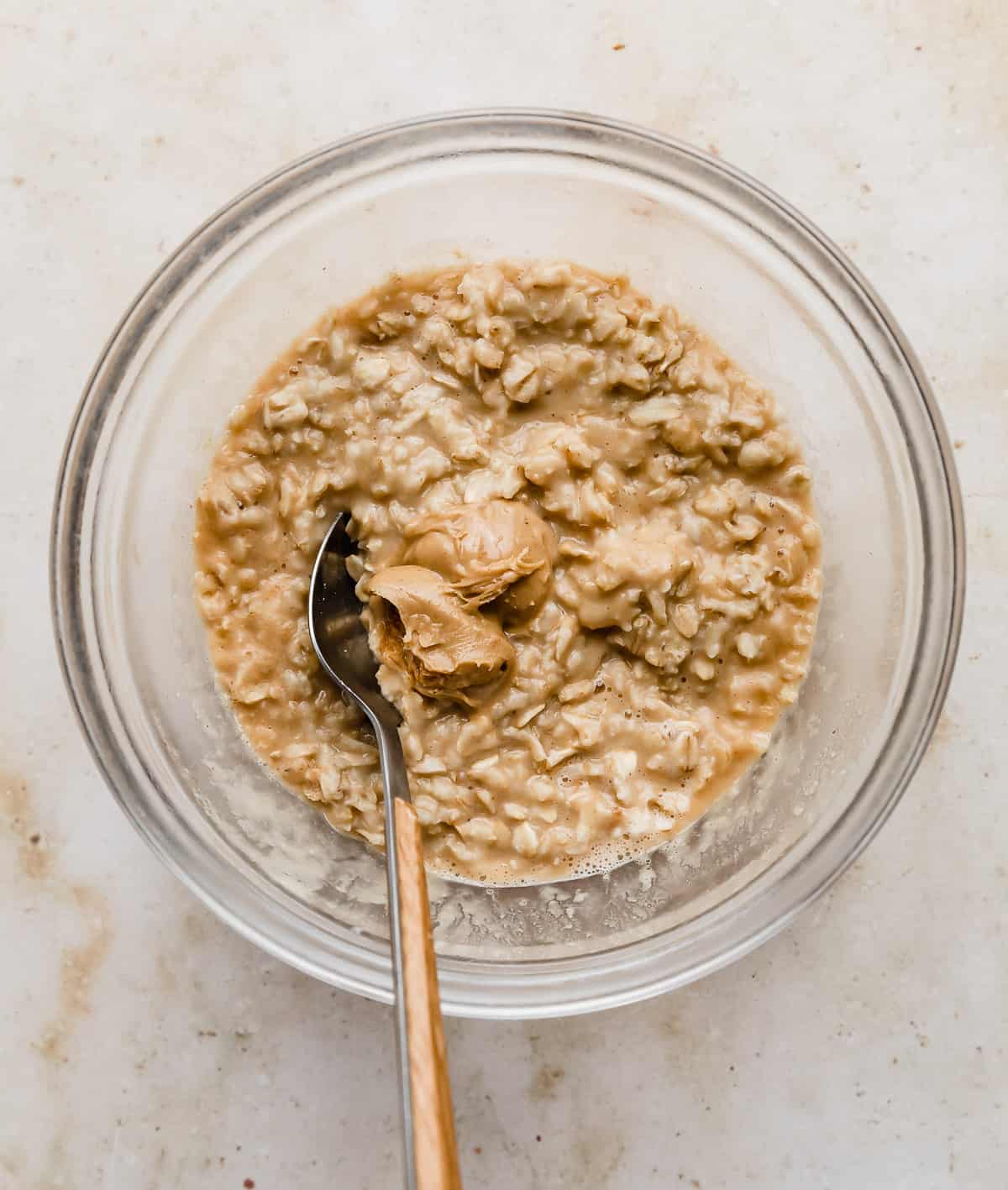A glass bowl with tan oatmeal and a dollop of peanut butter in it.