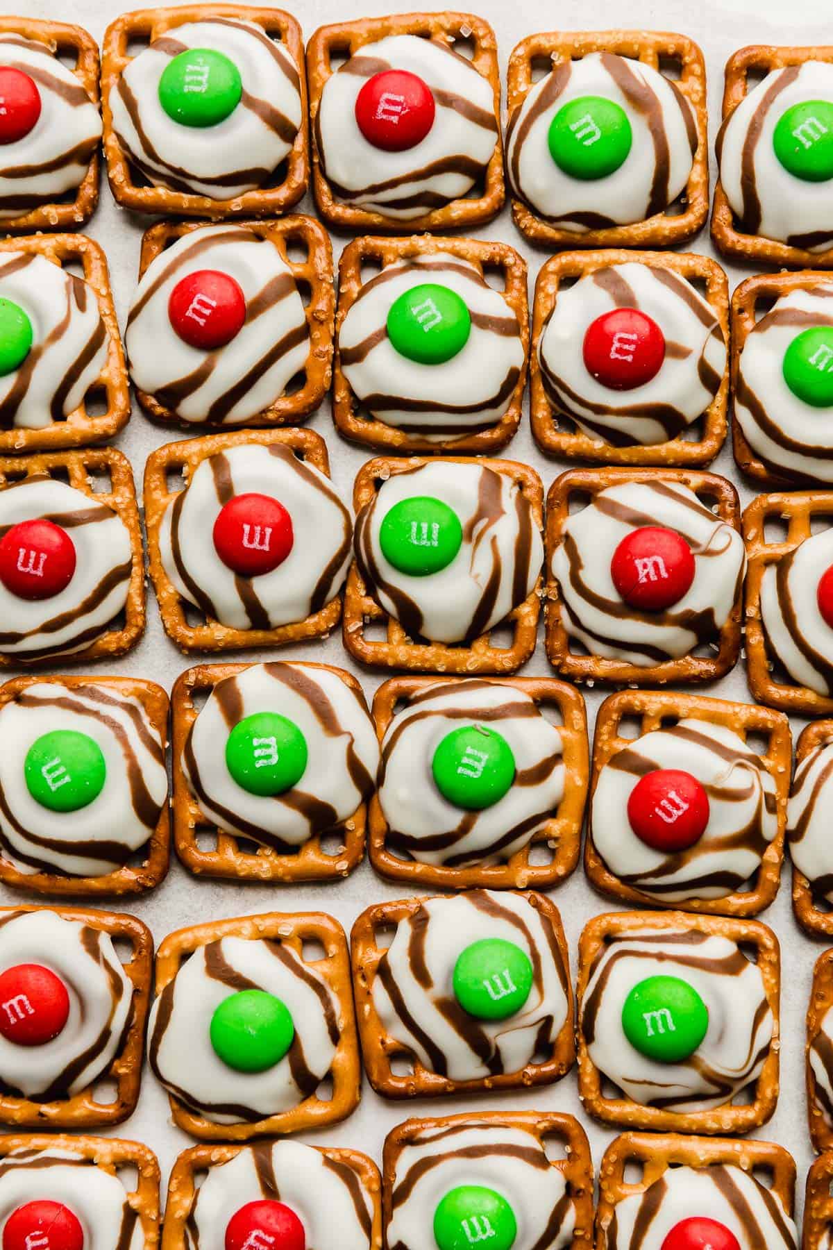 Red and green colored M&M's on top of melted hug candies on a square pretzel.