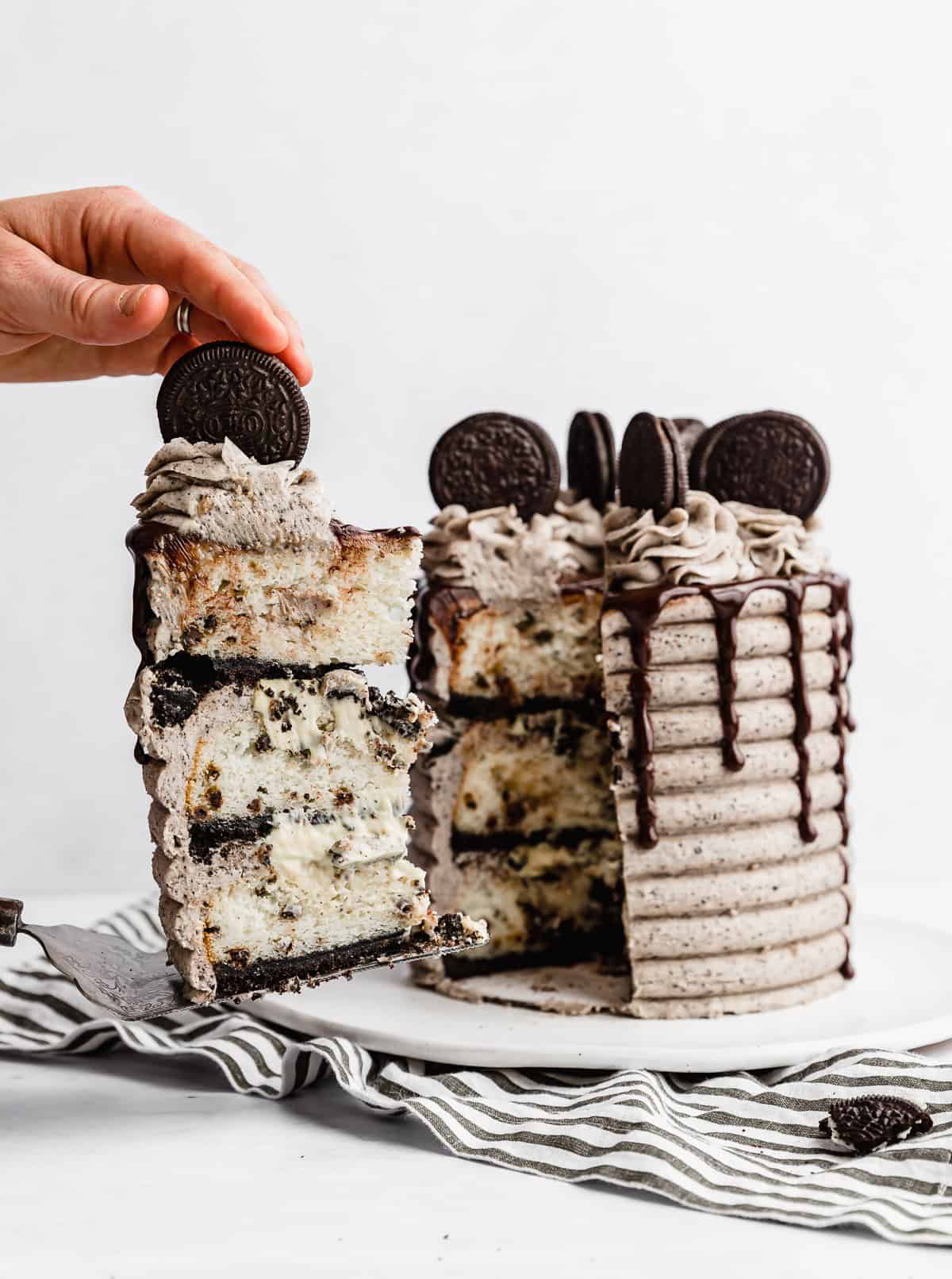 A slice of Coconut Cookies and Cream Cake against a white background with the main cake behind the slice.