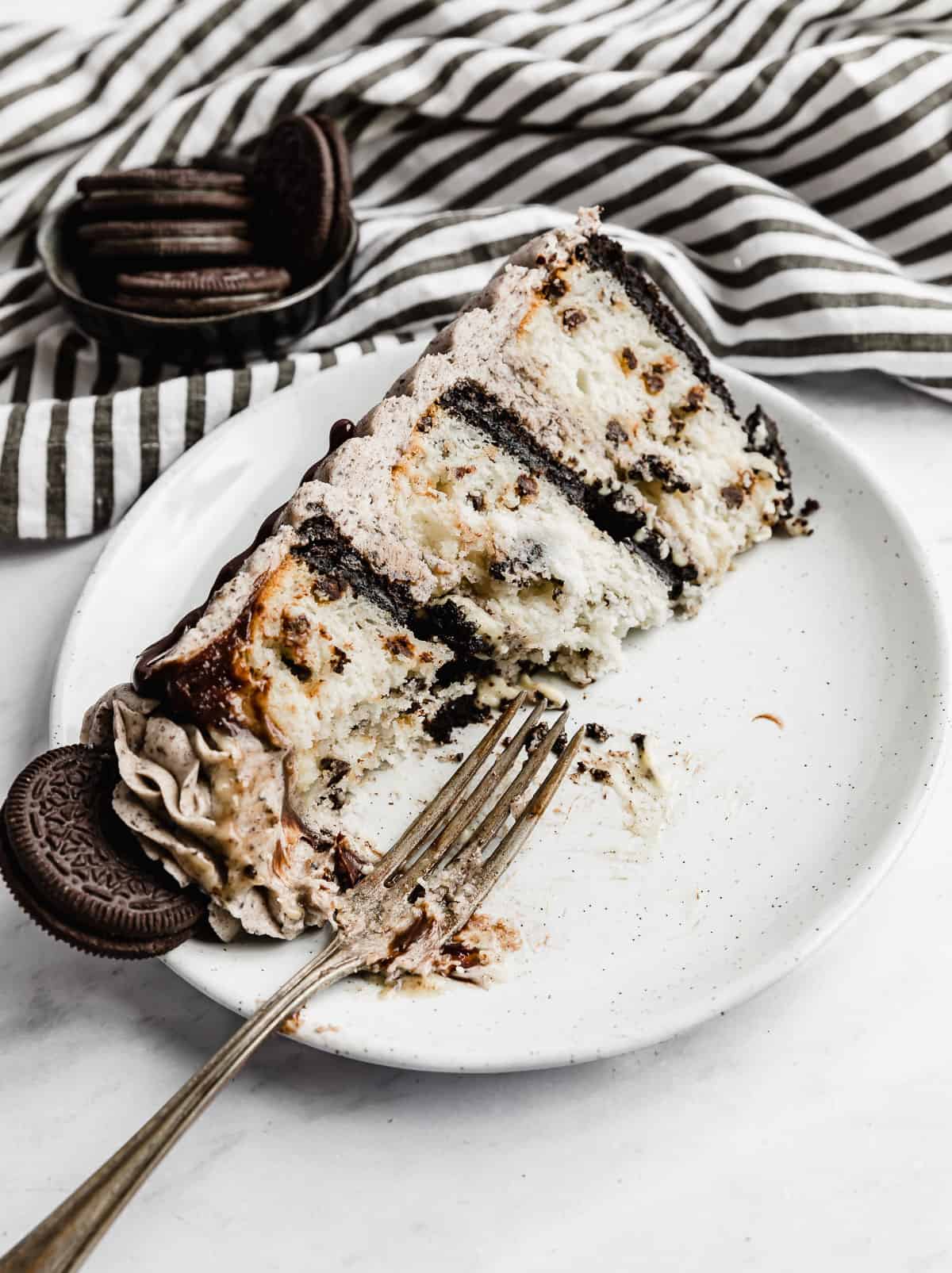 A slice of Coconut Cookies and Cream Cake on a white plate with a fork next to it.