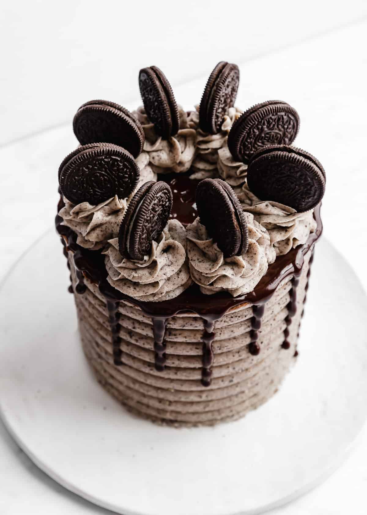 A Coconut Cookies and Cream Cake topped with chocolate ganache, frosting swirls, and Oreo cookies.