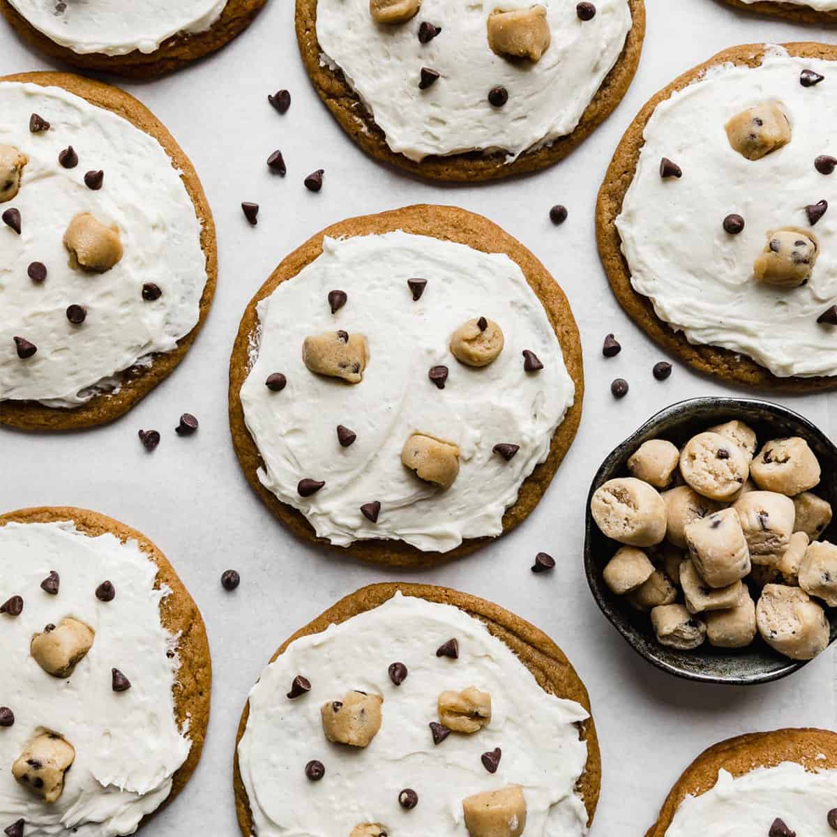 Crumbl Cookie Dough Cookies topped with white ice cream flavored frosting, mini chocolate chips, and edible cookie dough bites.