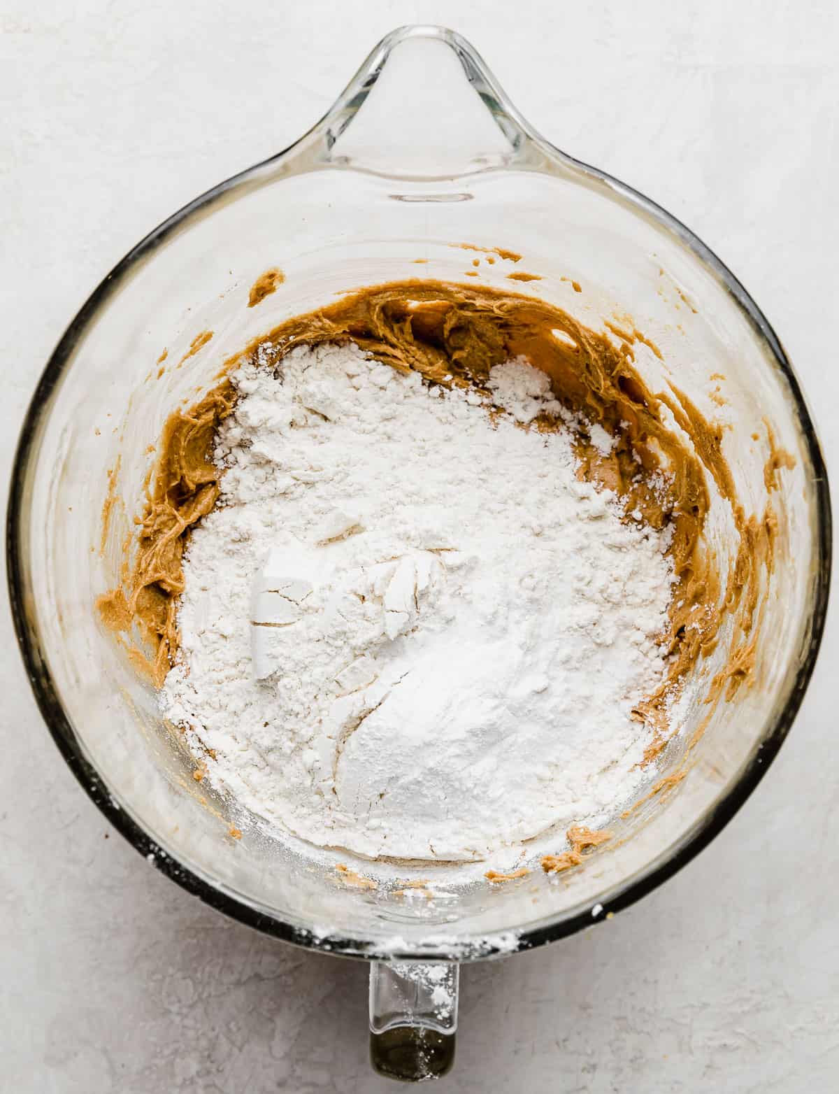 A white flour mixture on top of a deep brown colored creamed butter and sugar mixture.