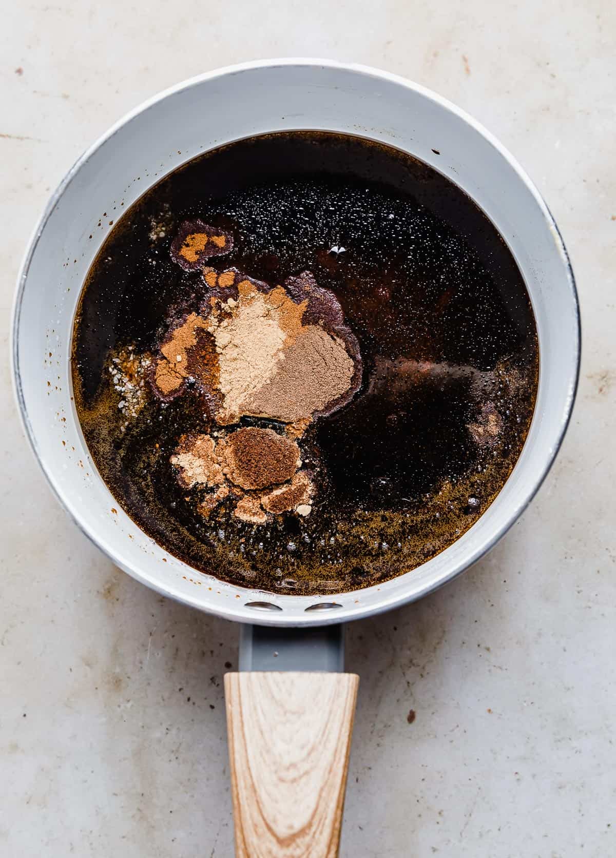 A dark liquid mixture in a white saucepan with gingerbread spices on top of the liquid.