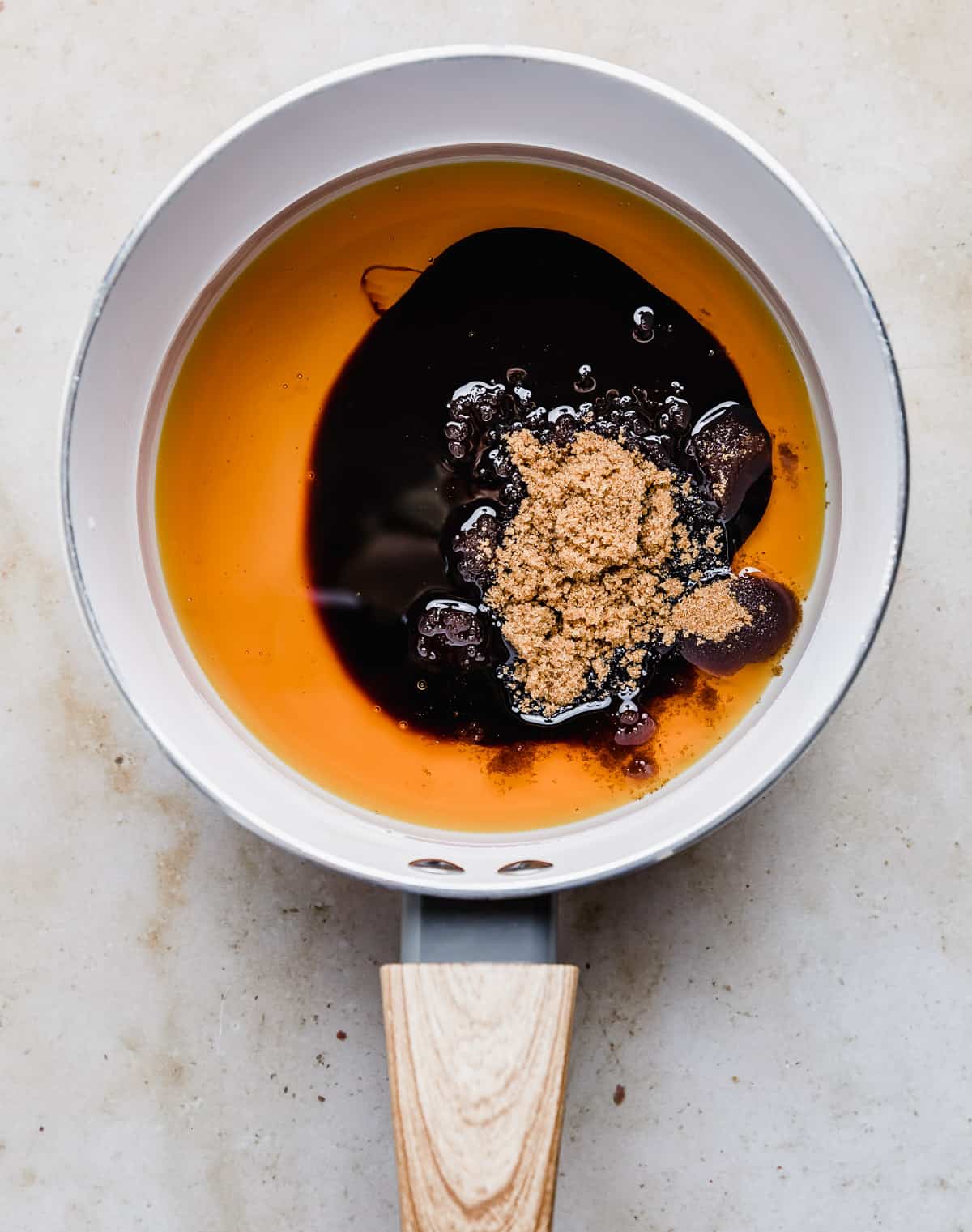 A white saucepan with oil, honey, molasses, and brown sugar in it.
