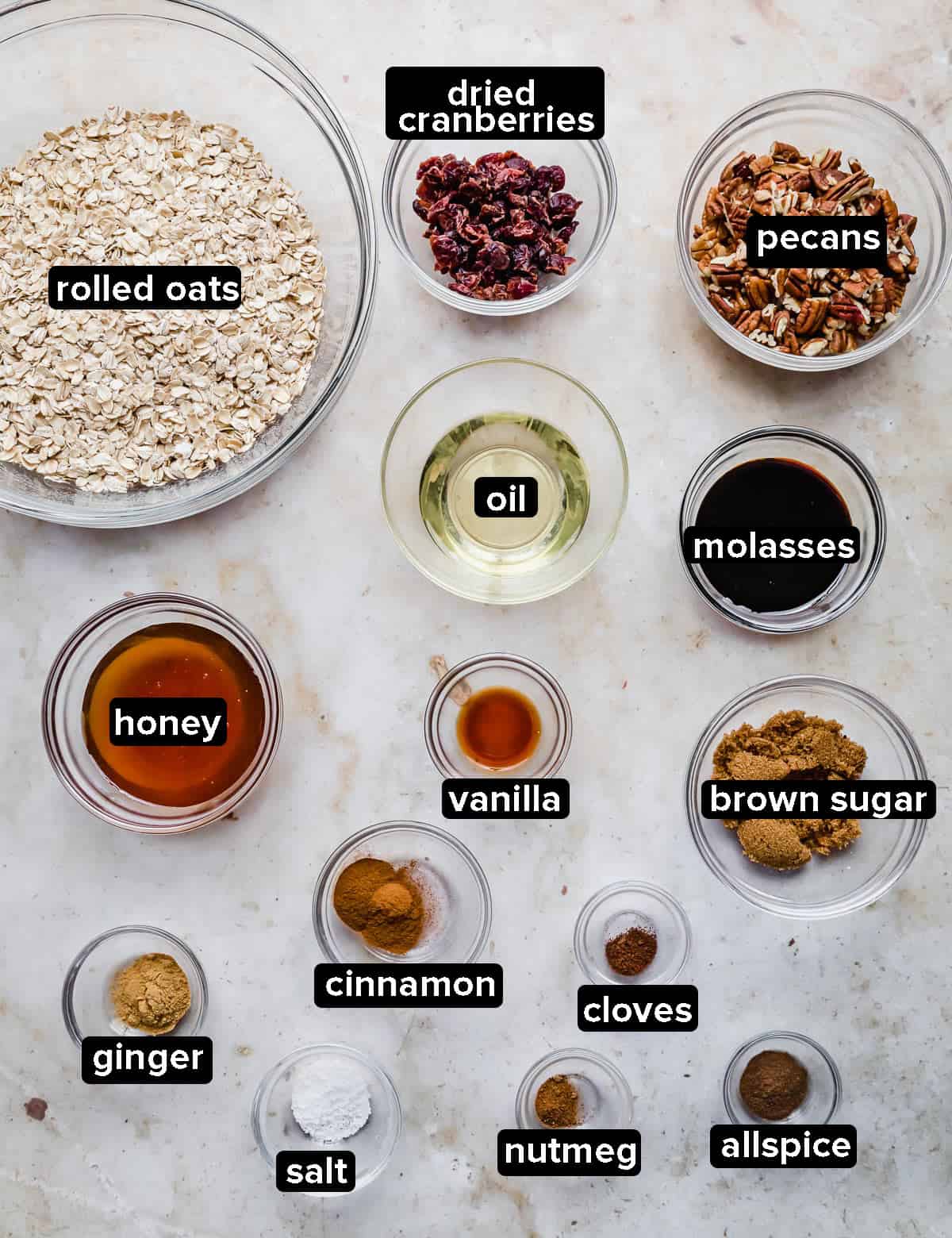 Gingerbread Granola ingredients in glass bowls on a gray textured background.