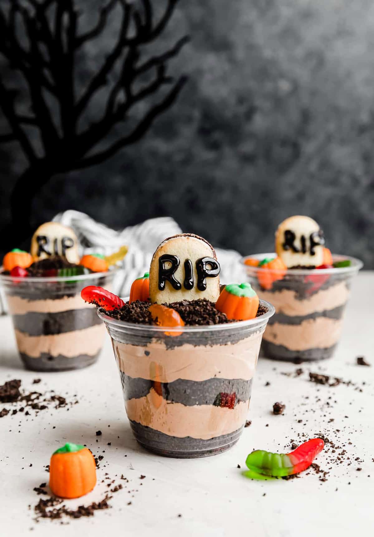 Halloween Dirt Cups topped with Oreo crumbs, gummy worms, and pumpkin shaped candy.