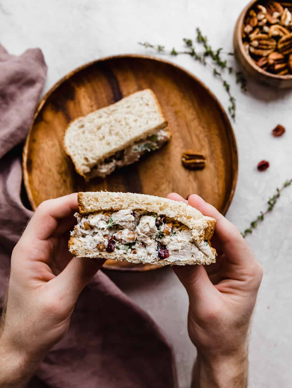 A hand holding a slice of Leftover Cranberry Turkey Salad Sandwich overtop of a gray background.