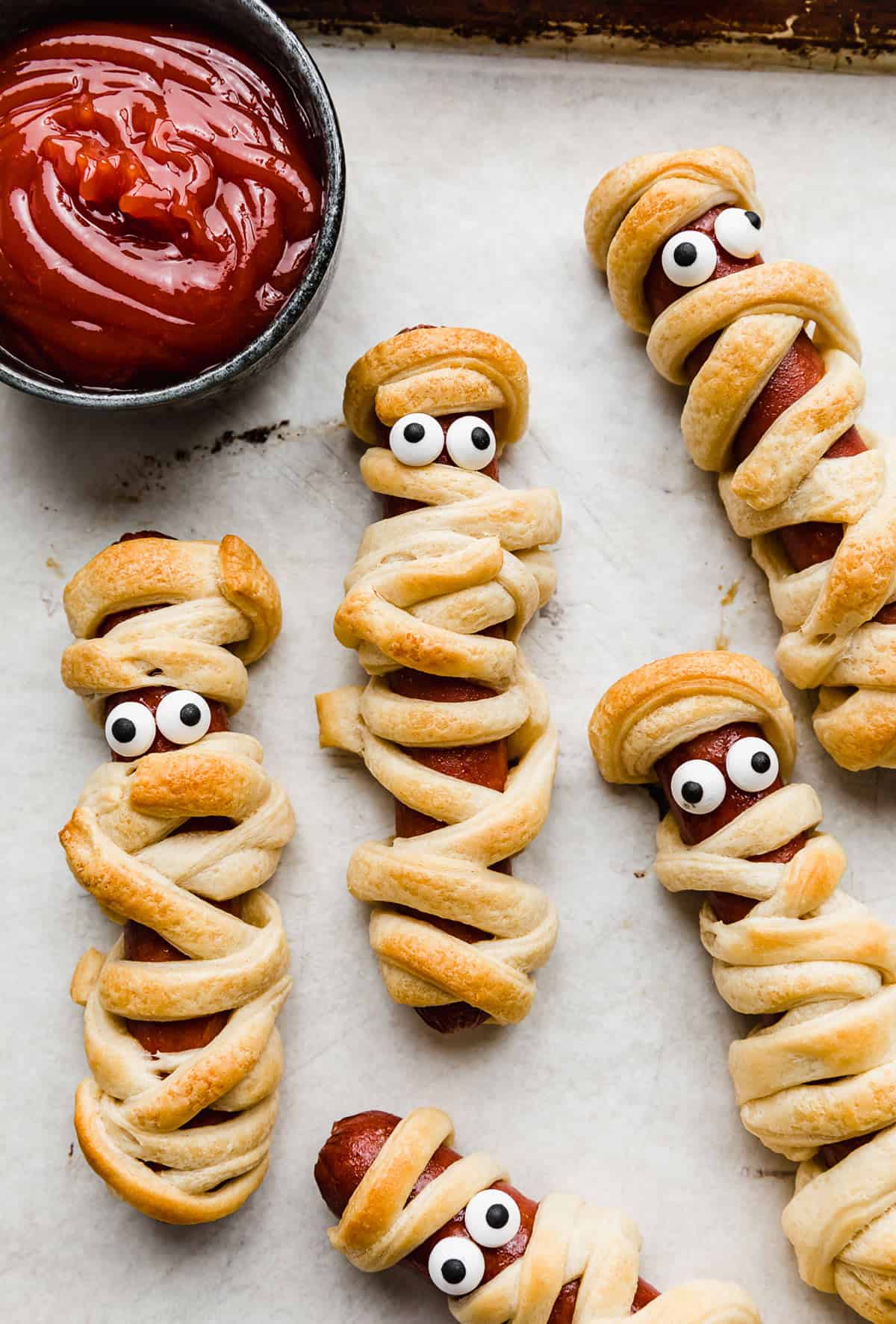 Mummy Hot Dogs on a parchment lined baking sheet with candy eyes on the hot dog.