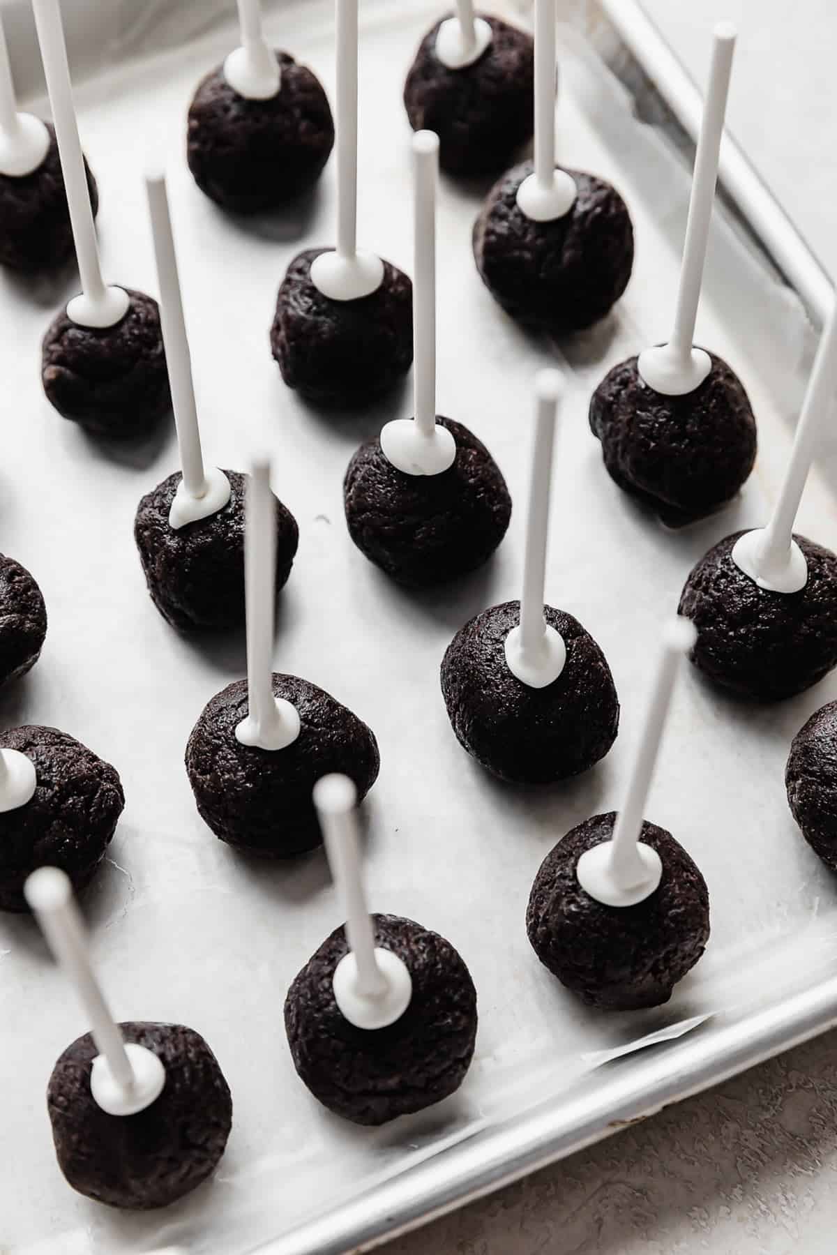 Oreo Cake Pop balls on a parchment lined baking sheet with white lollipop sticks in each Oreo pop.