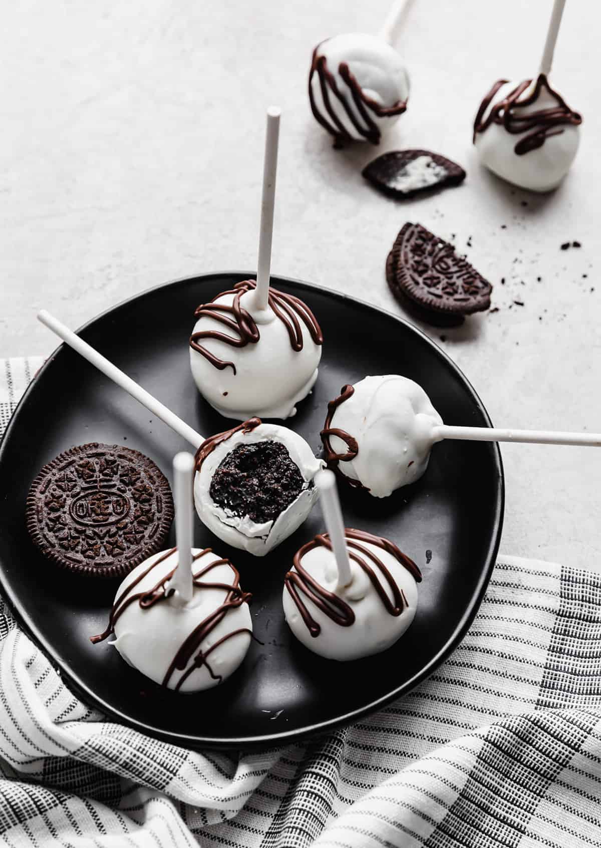 Oreo Cake Pops on a black plate with one having a bite taken out of it.