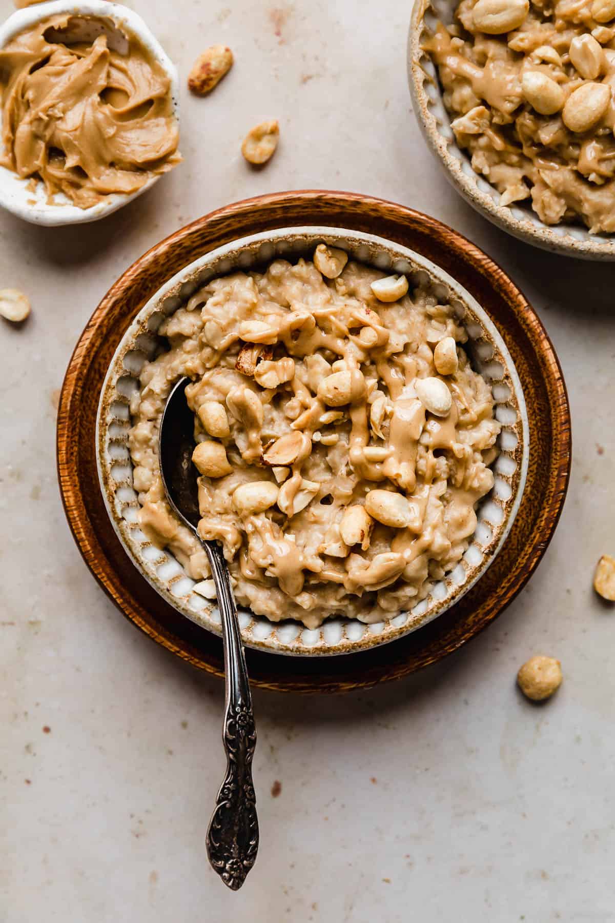 Peanut Butter Oatmeal topped with chopped peanuts in a tan bowl on a brown plate.