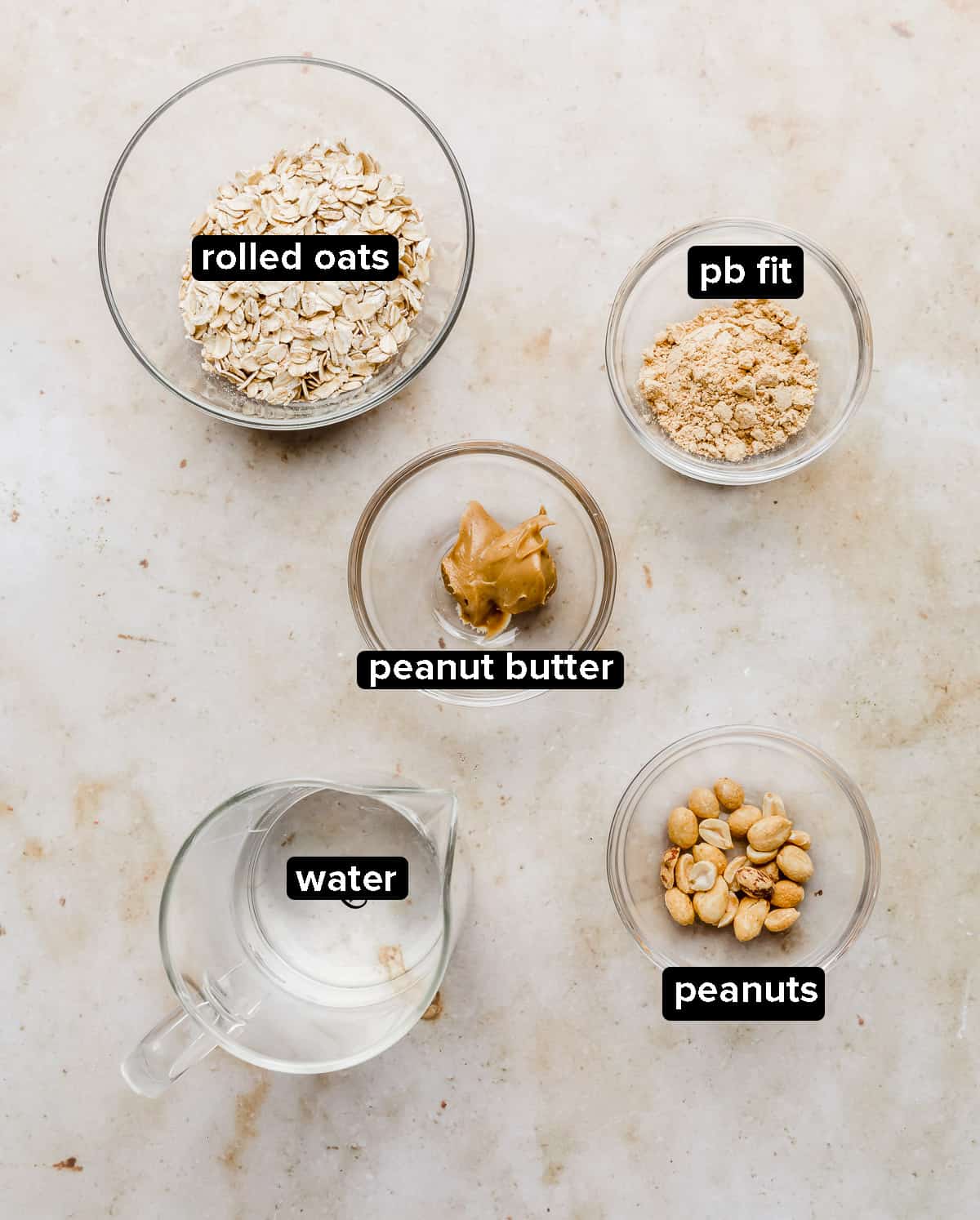 Peanut Butter Oatmeal ingredients in glass bowls on a tan marble background.