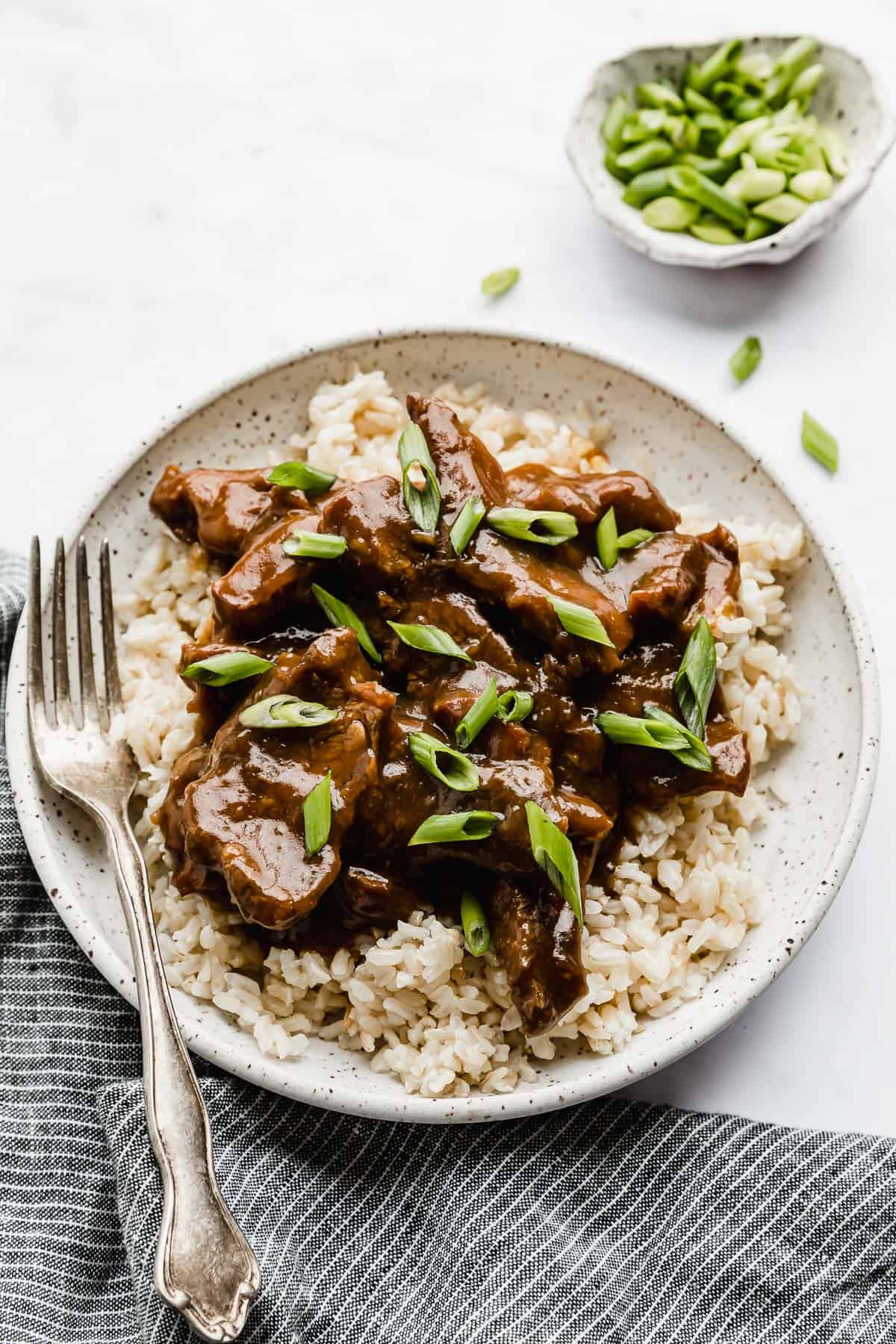 A white plate full of Slow Cooker Mongolian Beef on  bed of brown rice.