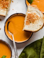 Zupas Tomato Basil Soup in a bowl with grilled cheese on the corner of the bowl.