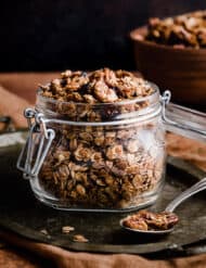 Gingerbread Granola in a glass jar against a black background.