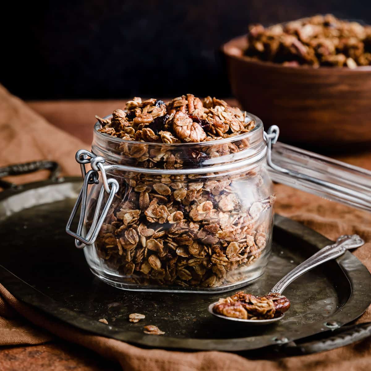 Gingerbread Granola in a glass jar against a black background.