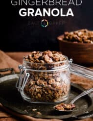 Gingerbread Granola in a glass jar sitting on a metal tray against a black background.