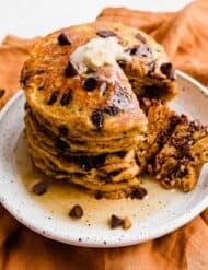 Pumpkin Chocolate Chip Pancakes on a white plate with a wedge of pancake cut out.
