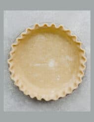 An All Butter Food Processor Pie Crust in a pie plate with fluted edges on a gray background.