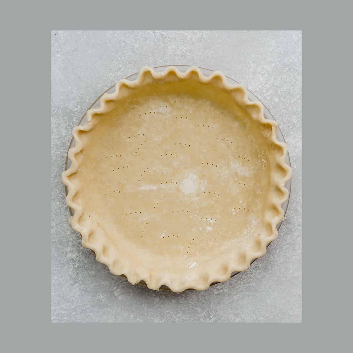 An All Butter Food Processor Pie Crust in a pie plate with fluted edges on a gray background.