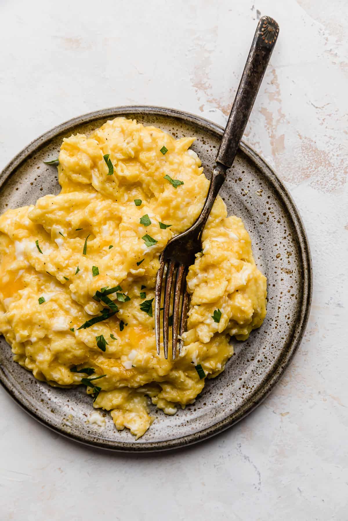 Cheesy Scrambled Eggs on a gray plate with a fork next to the eggs.