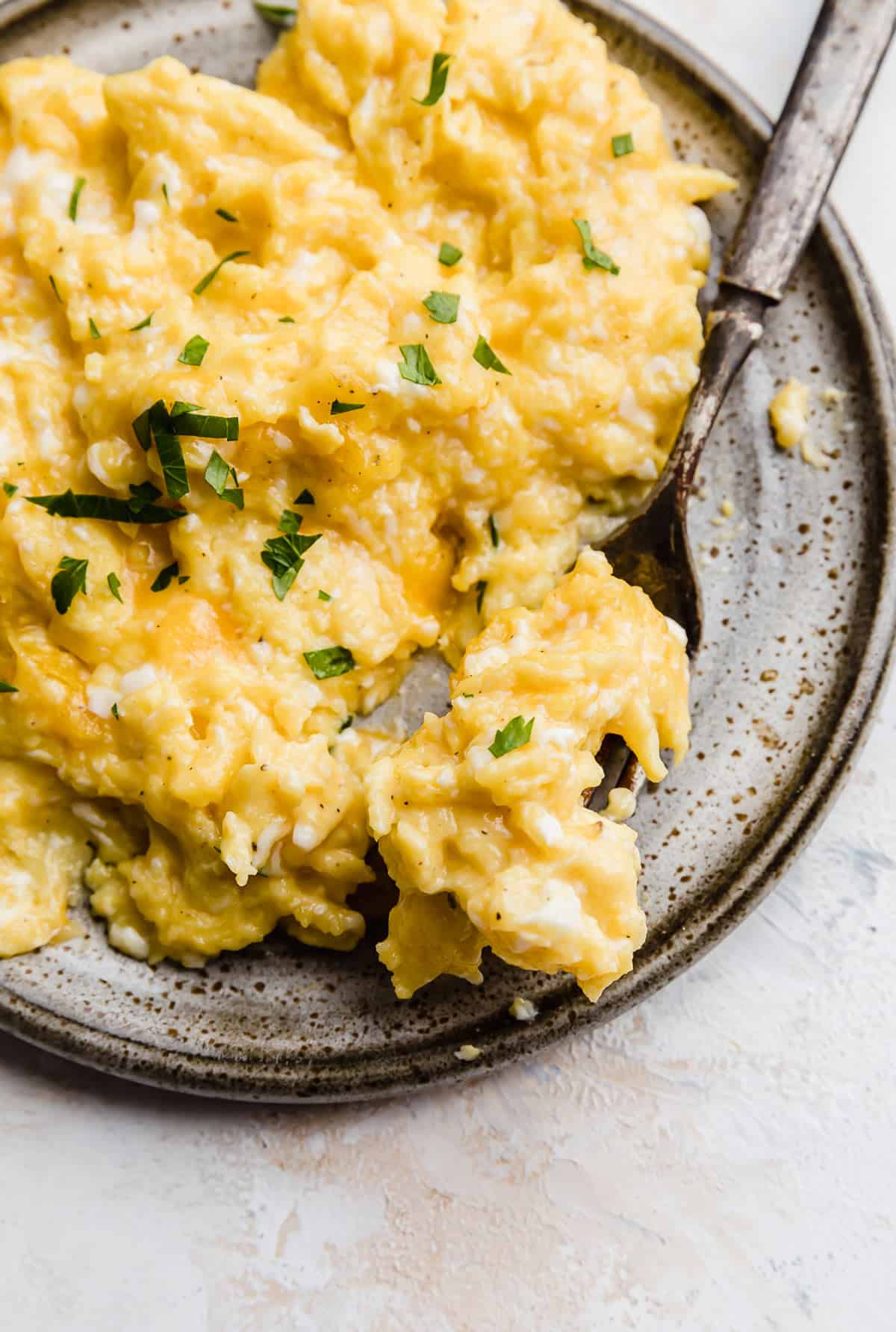 Close up photo of Cheesy Scrambled Eggs topped with fresh parsley.