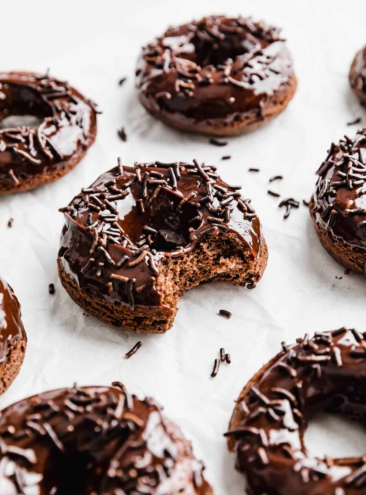 Baked Chocolate Doughnuts topped with chocolate sprinkles, with a bite taken out of one doughnut.