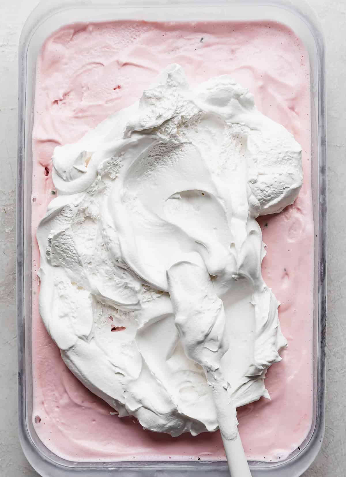 White cool whip portioned in the center of pink peppermint ice cream in a rectangular dish.